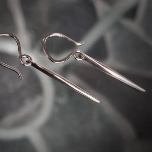 May include: A pair of silver earrings with a simple, minimalist design. Each earring features a thin, straight wire that extends from a small, curved hook.