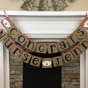 May include: A brown paper banner with red string and white nurse hats with red crosses. The banner reads "Congrats Nurse Jenny".
