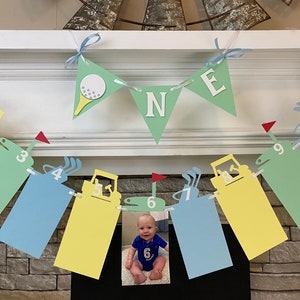 May include: A green, yellow, and blue paper banner with a golf theme. The banner has the word 