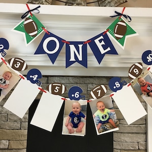 May include: A blue and white 'ONE' banner with football-themed decorations and photos of a baby boy for a first birthday party.