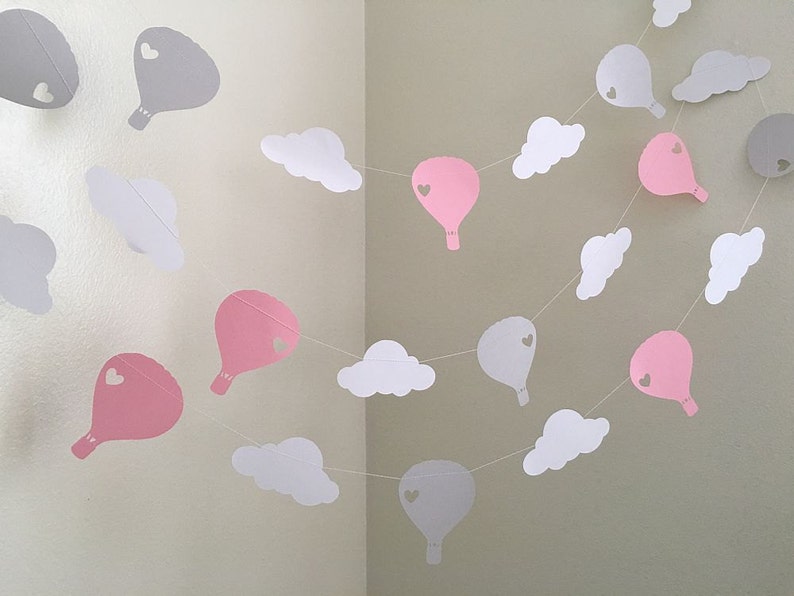 Puede incluir: Una guirnalda de globos de papel rosa y gris y nubes de papel blanco. Los globos tienen un peque&ntilde;o coraz&oacute;n recortado en el centro.