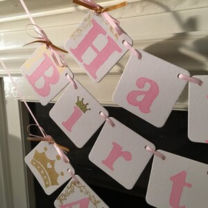 May include: Pink and gold happy birthday banner with a crown on the letter "i".
