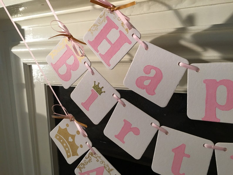 May include: Pink and gold happy birthday banner with a crown on the letter "i".