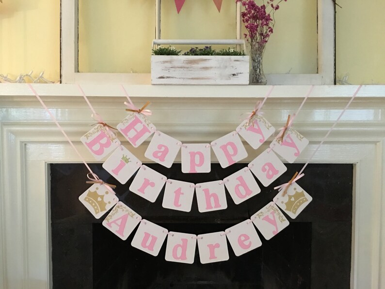 May include: Pink and gold banner with the words "Happy Birthday Audrey". The banner is made of cardstock and has a crown design on each end.