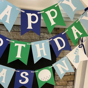 May include: Happy Birthday banner with blue, green, and white flags. The flags have the letters "Happy Birthday" and a golf ball and golf clubs.
