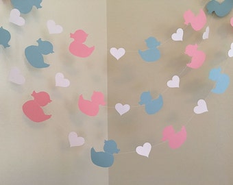 May include: A garland with alternating pink and blue duck silhouettes and white hearts. The garland is strung on a clear string.