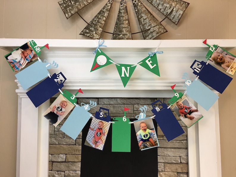 May include: A green, blue, and white banner with the word "ONE" in green letters. The banner is decorated with golf carts and golf balls. There are photos of a baby boy in each of the banner's sections.