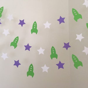 May include: A green and purple paper garland with rockets and stars. The garland is perfect for a space-themed party.