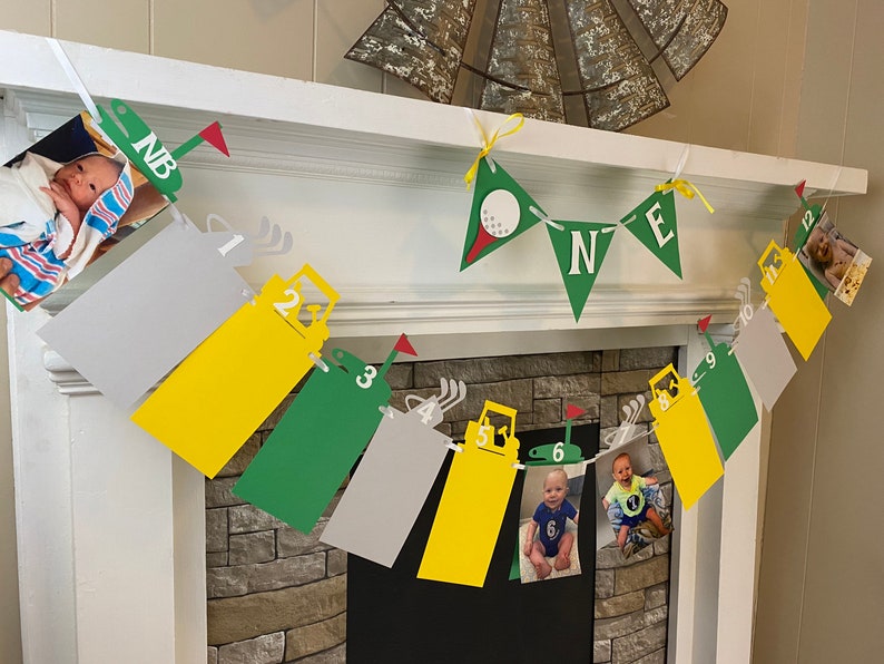 May include: A green, yellow, and gray banner with photos of a baby boy at different ages. The banner has a golf theme with golf carts and golf balls. The banner says "NB" and "ONE".