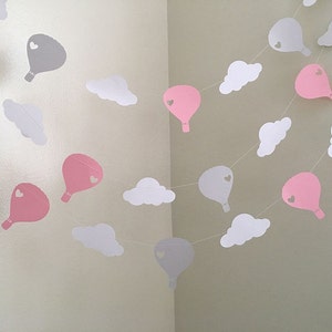 Puede incluir: Una guirnalda de globos de papel rosa y gris y nubes de papel blanco. Los globos tienen un peque&ntilde;o coraz&oacute;n recortado en el centro.