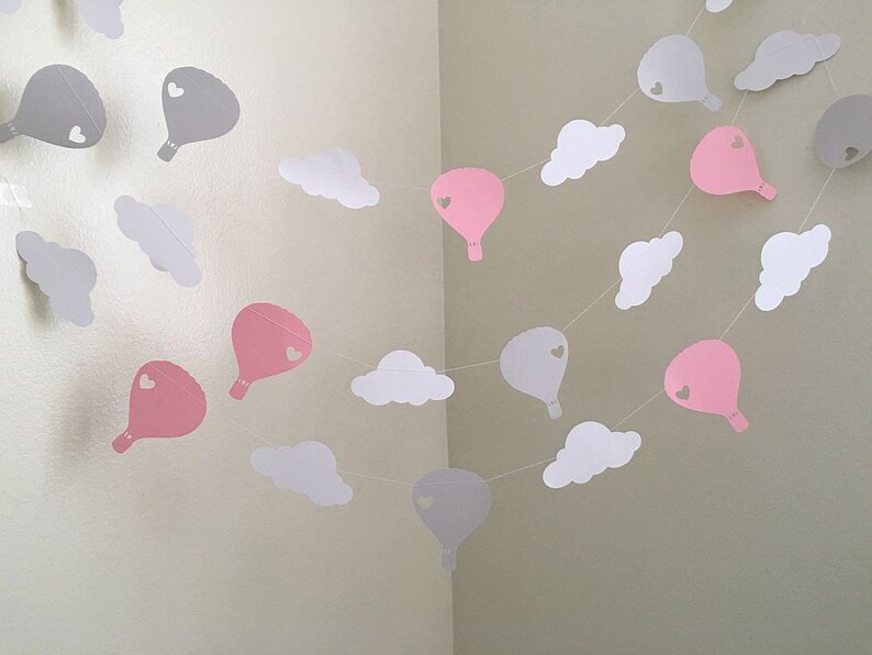 Puede incluir: Una guirnalda de globos de papel rosa y gris y nubes de papel blanco. Los globos tienen un peque&ntilde;o coraz&oacute;n recortado en el centro.