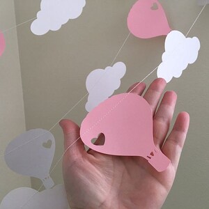 Puede incluir: Guirnalda de papel rosa y blanca con globos aerost&aacute;ticos y nubes. La guirnalda est&aacute; enhebrada con hilo blanco.