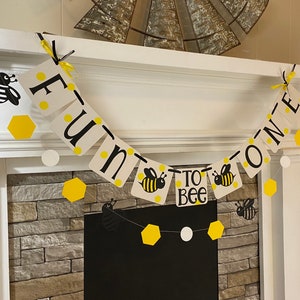 May include: A yellow and black bee-themed banner with the text "Fun to Bee One". The banner is decorated with yellow hexagons and white circles.