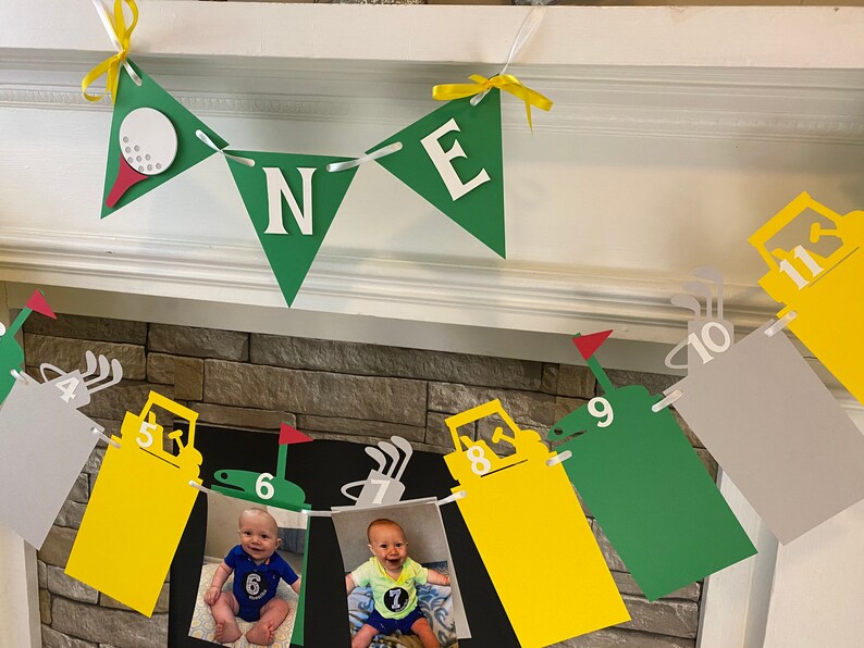 May include: A green and yellow golf-themed banner with the word "ONE" in white letters. The banner is decorated with golf balls, golf clubs, and a golf cart. There are also photos of a baby boy in the banner.