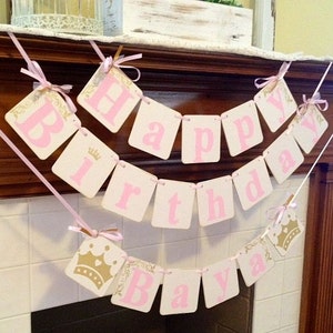 May include: A pink and white banner with gold accents reads "Happy Birthday Ava". The banner is strung across a white tiled fireplace mantel.