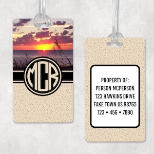 May include: A luggage tag with a sunset beach scene and the monogram "MCR" in a black circle. The back of the tag has a beige background with black text that reads "PROPERTY OF: PERSON MCPERSON 123 HAWKINS DRIVE FAKE TOWN US 98765 123 • 456 • 7890".