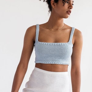 May include: A light blue knitted crop top with thin straps. The top is made of a soft, textured fabric and has a square neckline.