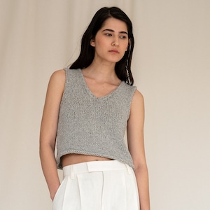 May include: A woman wearing a gray sleeveless knitted top and white wide-leg pants. She is standing on a white background.