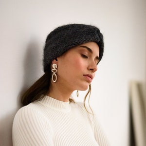 May include: A woman wearing a white ribbed sweater and a dark gray knit headband. She is wearing silver hoop earrings with a small circle charm.