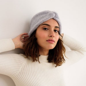 May include: A woman wearing a light purple knitted headband and a white ribbed sweater.
