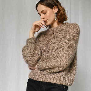 May include: A brown knitted sweater with a loose fit and long sleeves. The sweater is made of a soft, fuzzy yarn.