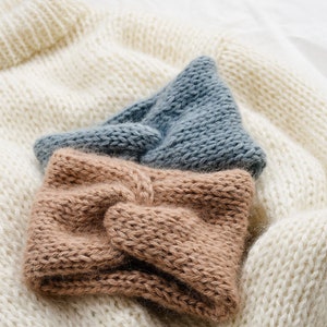 May include: Two knitted headbands, one brown and one blue, are stacked on top of a white knitted sweater.