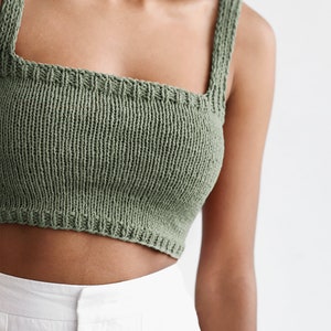 May include: A sage green knitted crop top with thin straps. The top is made of a soft, lightweight fabric and has a square neckline.