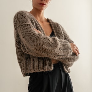 May include: A brown fuzzy knit cardigan with a v-neck and long sleeves. The cardigan is cropped and has a relaxed fit.