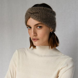 May include: A brown knitted headband with a criss-cross design. The headband is worn by a person with brown hair and is styled to cover the forehead.