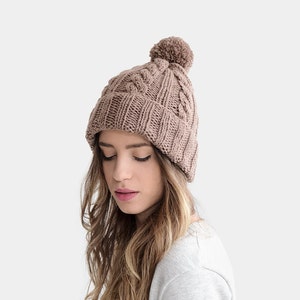May include: A brown knitted beanie with a pom pom on top. The beanie has a cable knit pattern.