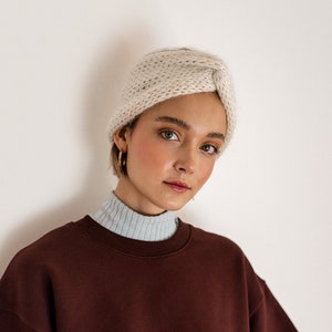 May include: A woman wearing a maroon sweatshirt with a white knit headband. The sweatshirt has a relaxed fit and a cropped length.
