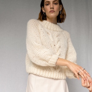 May include: A white cable knit sweater with a relaxed fit and a white leather skirt.