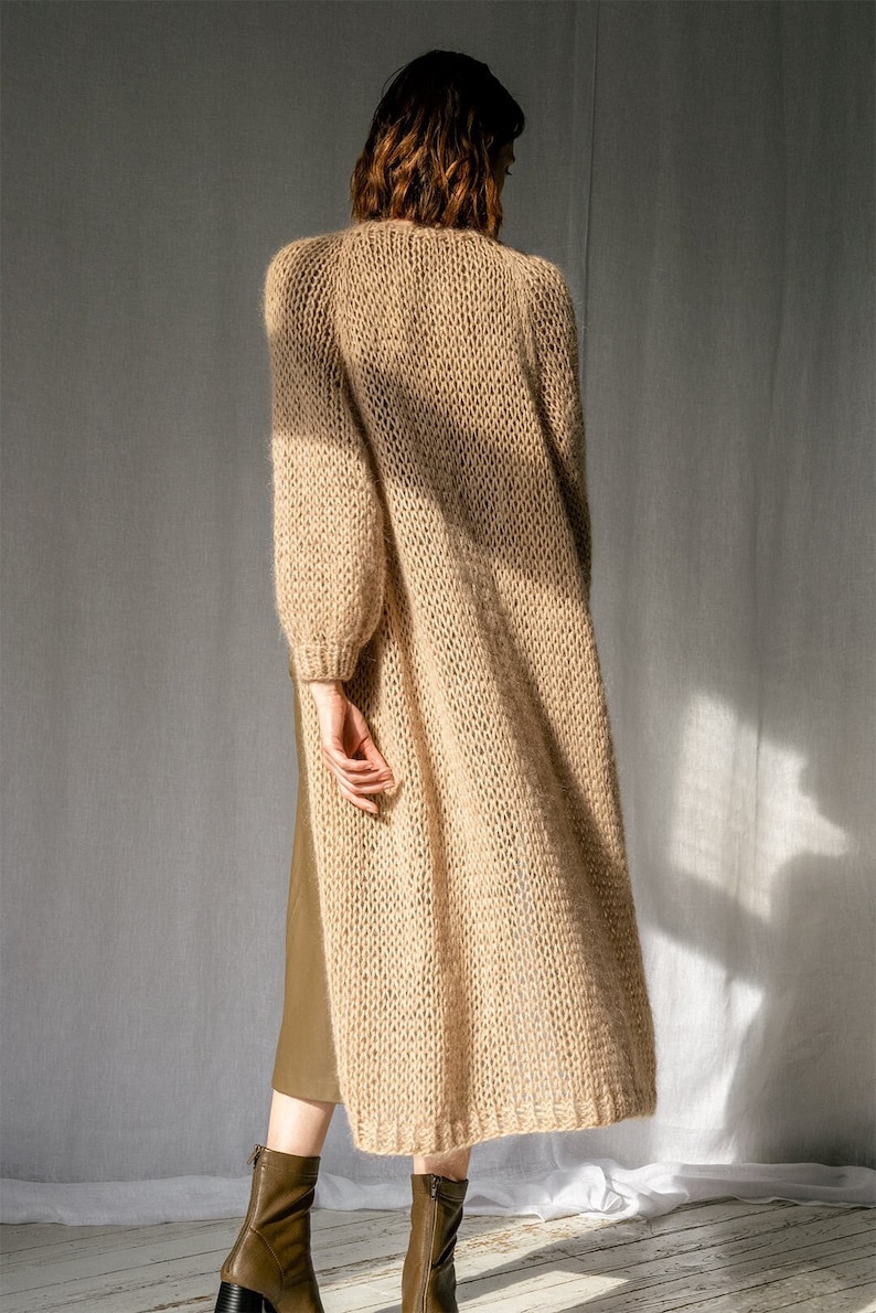 K&ouml;nnte beinhalten: Ein langer, beiger Cardigan mit lockerer Passform und gestrickter Textur. Der Cardigan ist aus weichem, flauschigem Garn gefertigt und hat einen l&auml;ssigen, entspannten Stil.