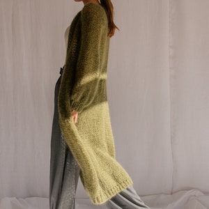 K&ouml;nnte beinhalten: Ein langer, olivgr&uuml;ner Cardigan mit lockerer Passform und leicht offenem Vorderteil. Der Cardigan ist aus einem weichen, flauschigen Material gefertigt und hat einen l&auml;ssigen, entspannten Stil.
