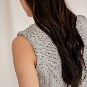May include: A gray sleeveless knitted top with a loose fit. The top is made of a soft, textured fabric.