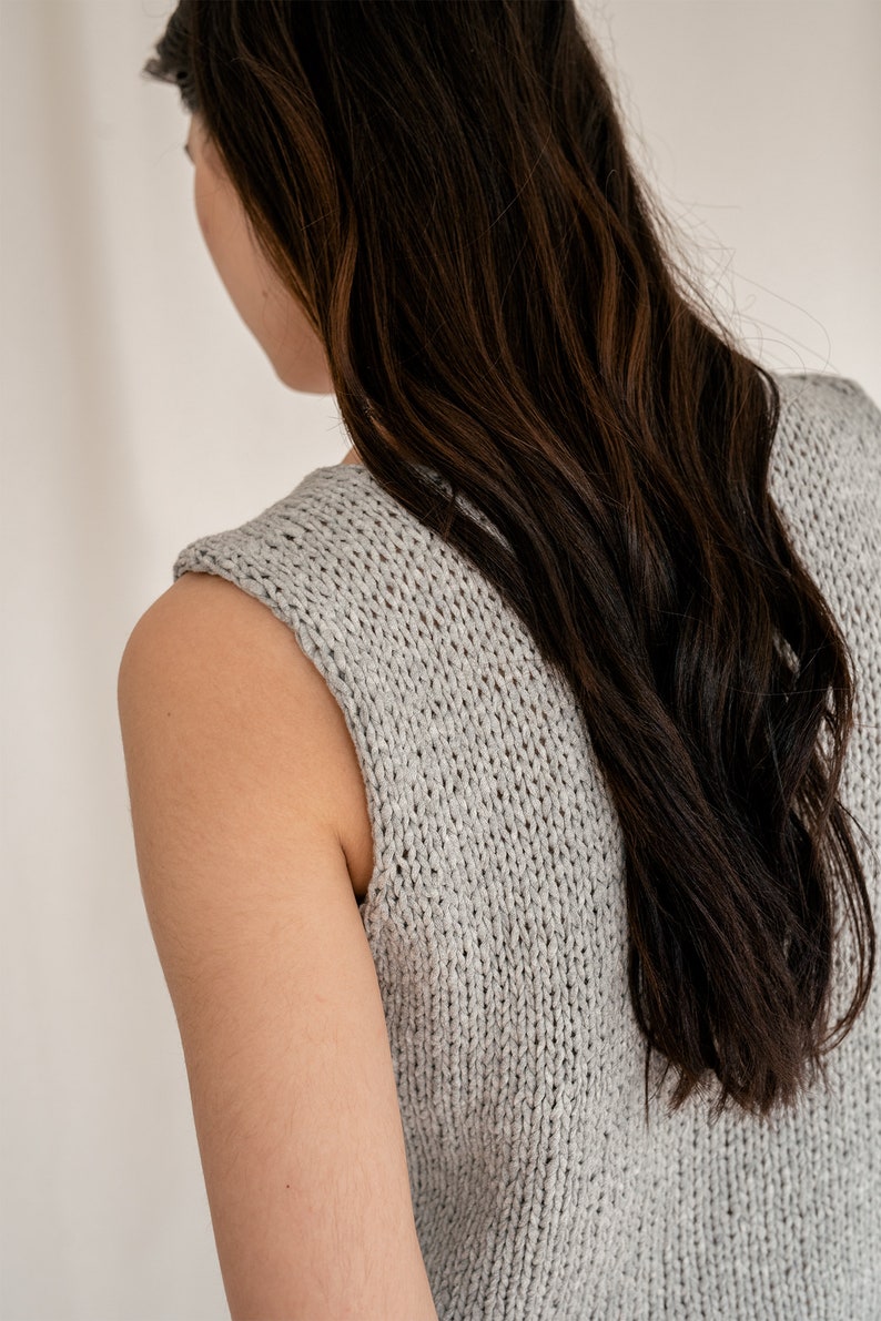 May include: A gray sleeveless knitted top with a loose fit. The top is made of a soft, textured fabric.