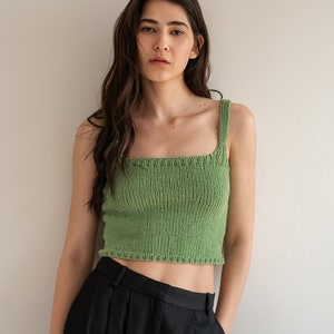 May include: A woman wearing a green knitted crop top and black high-waisted pants.