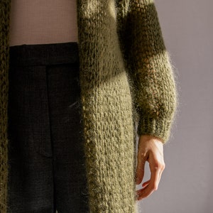 K&ouml;nnte beinhalten: Ein langer, gr&uuml;ner, flauschiger Cardigan mit lockerer Passform und langen &Auml;rmeln. Der Cardigan ist aus einem weichen, gestrickten Stoff gefertigt und hat einen l&auml;ssigen, entspannten Stil.