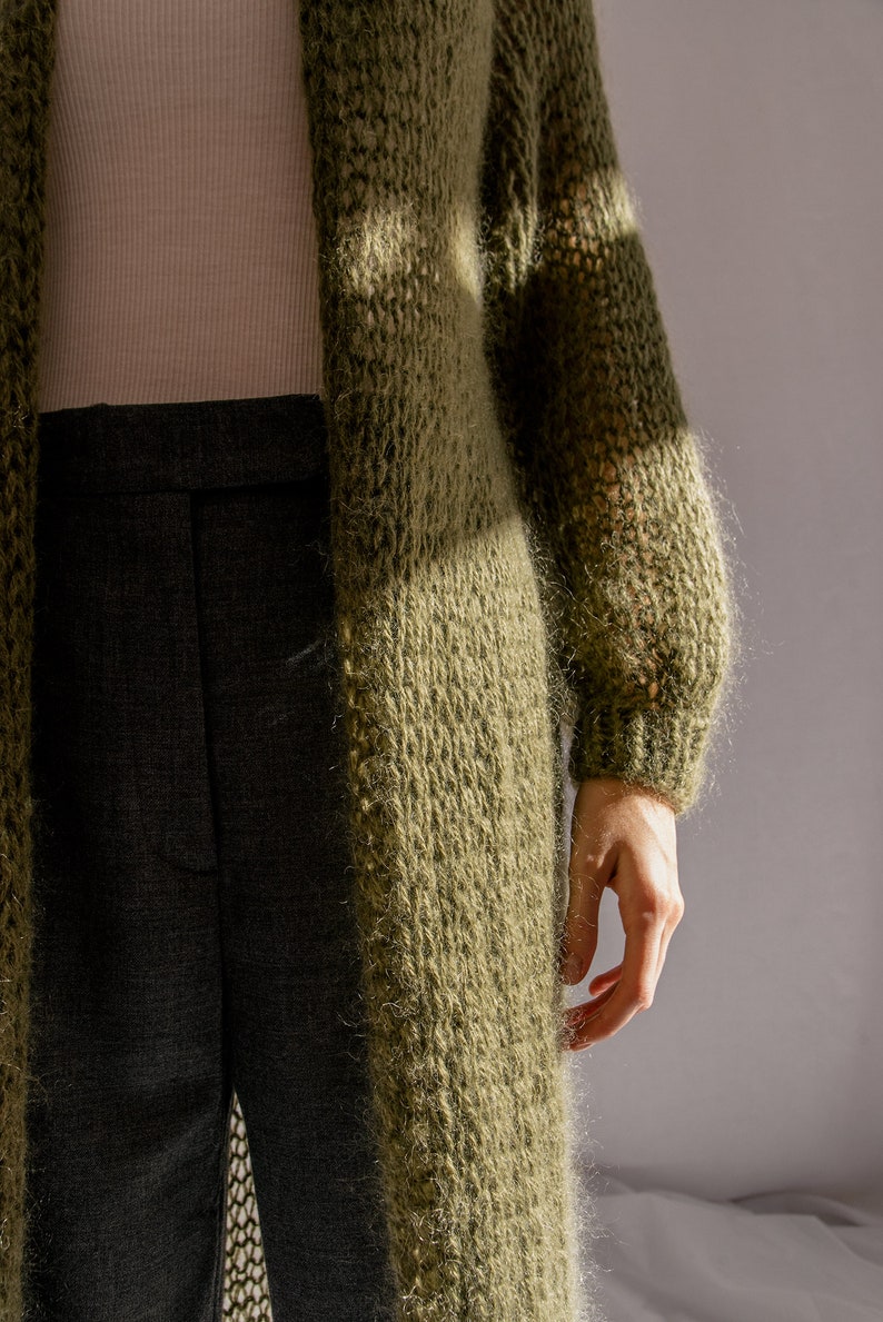 K&ouml;nnte beinhalten: Ein langer, gr&uuml;ner, flauschiger Cardigan mit lockerer Passform und langen &Auml;rmeln. Der Cardigan ist aus einem weichen, gestrickten Stoff gefertigt und hat einen l&auml;ssigen, entspannten Stil.