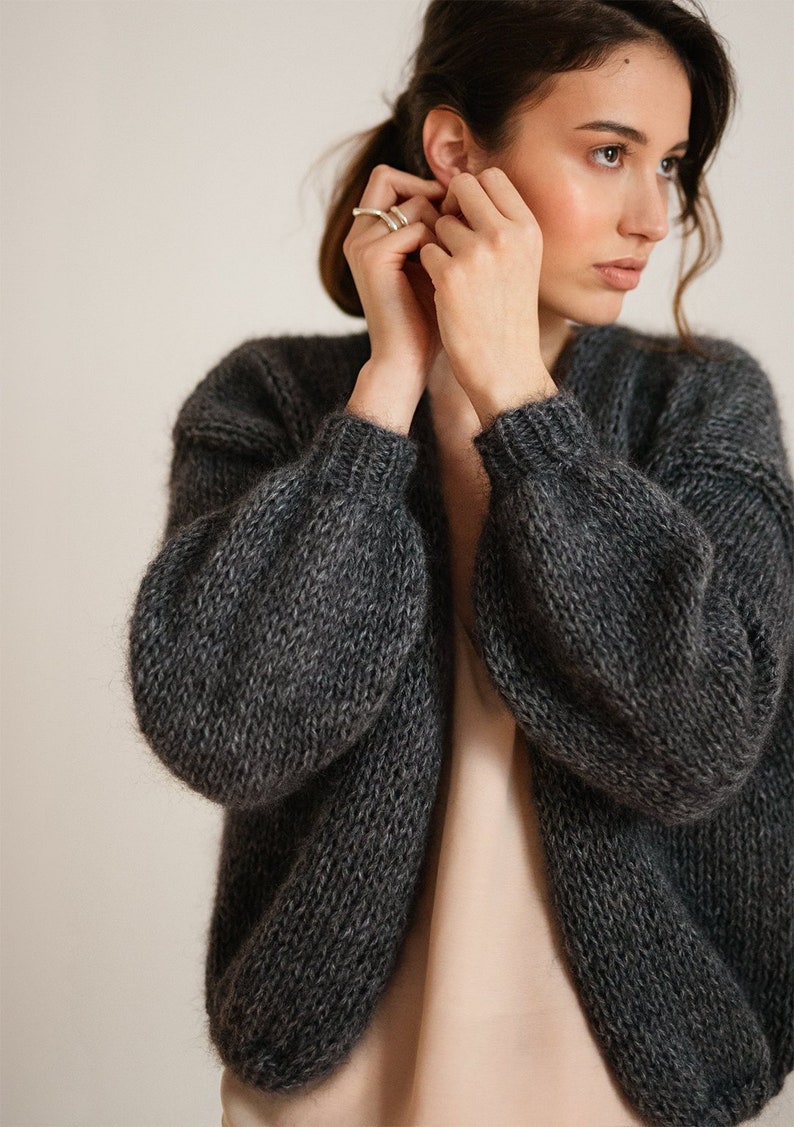 Peut inclure: Un cardigan en tricot gris fonc&eacute; &agrave; manches longues et col en V. Le cardigan est fait d'un fil doux et duveteux.