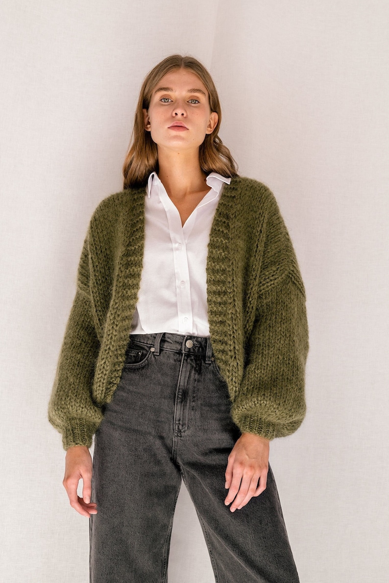 Peut inclure: Un cardigan en tricot vert &agrave; la coupe ample et aux manches longues. Le cardigan est ouvert sur le devant et a un col en V.