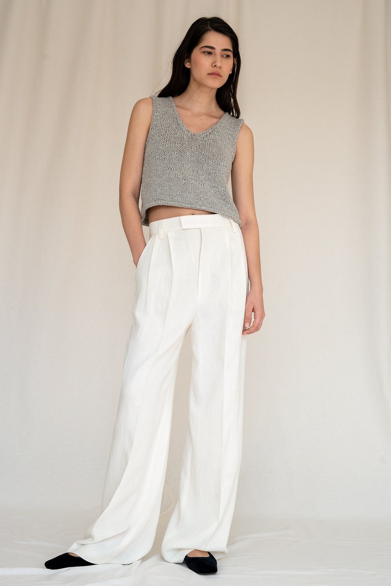 May include: A woman wearing a gray sleeveless knitted top and white wide-leg pants. She is standing on a white background.