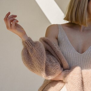 Peut inclure: Un cardigan en tricot marron clair &agrave; manches longues et &agrave; la coupe ample. Le cardigan est fait d'un fil doux et moelleux et a un style d&eacute;contract&eacute; et d&eacute;tendu.