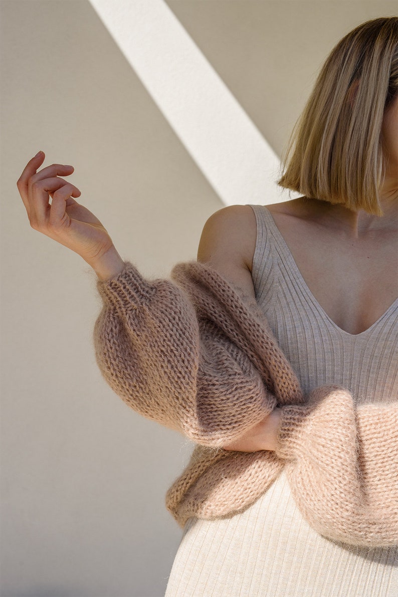 Peut inclure: Un cardigan en tricot marron clair &agrave; manches longues et &agrave; la coupe ample. Le cardigan est fait d'un fil doux et moelleux et a un style d&eacute;contract&eacute; et d&eacute;tendu.