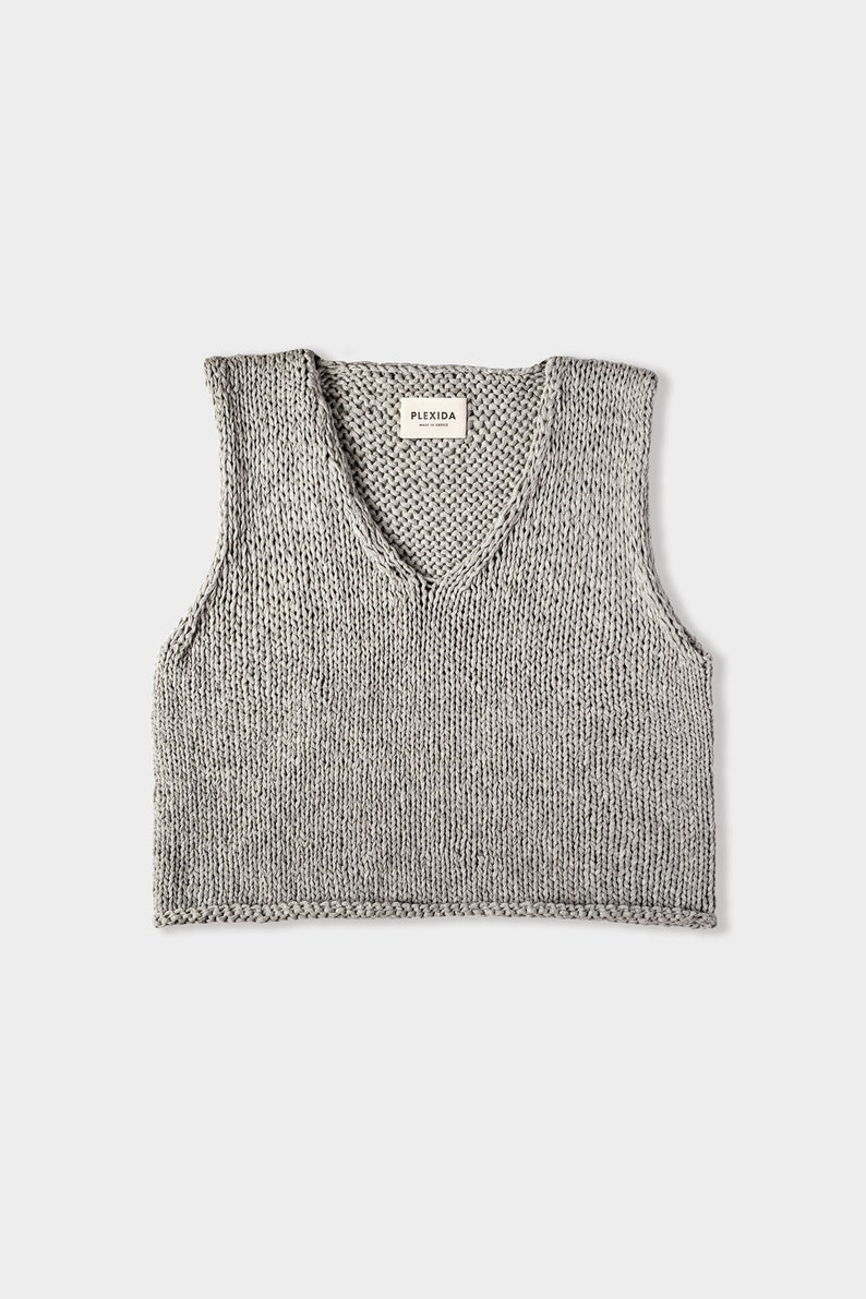 May include: A gray knitted sleeveless vest with a V-neck and a small label that says "PLEXIDA" in the center of the neckline.