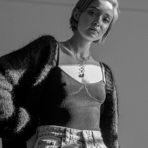Peut inclure: Une femme portant un cardigan en fourrure noire sur un d&eacute;bardeur c&ocirc;tel&eacute; noir et un jean bleu clair. Elle porte un collier en cha&icirc;ne argent avec un pendentif.