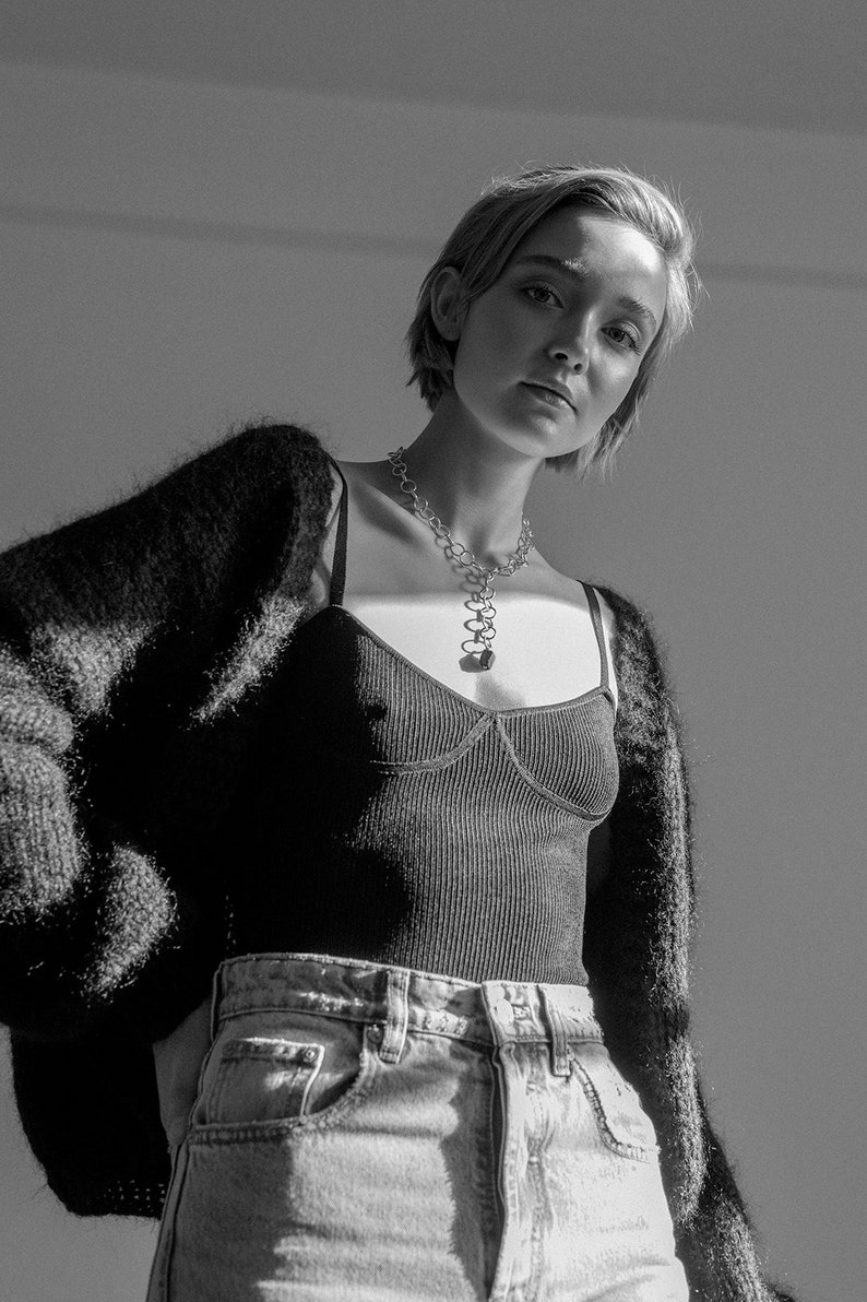 Peut inclure: Une femme portant un cardigan en fourrure noire sur un d&eacute;bardeur c&ocirc;tel&eacute; noir et un jean bleu clair. Elle porte un collier en cha&icirc;ne argent avec un pendentif.