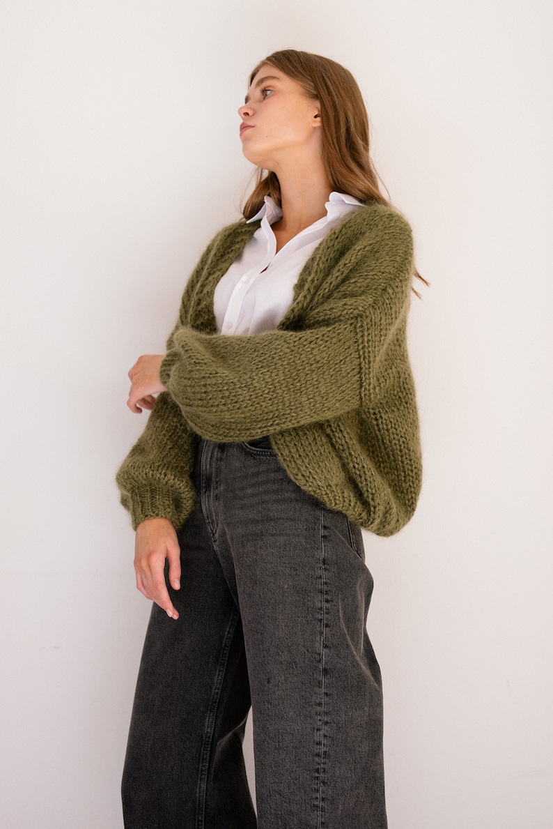 Peut inclure: Une femme portant un cardigan en tricot vert avec une chemise boutonn&eacute;e blanche en dessous et un jean fonc&eacute;.