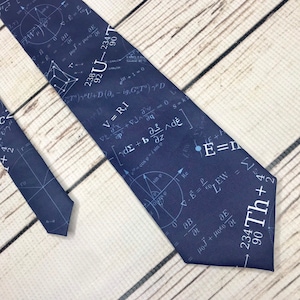 May include: Navy blue necktie featuring a repeating pattern of white mathematical equations, formulas, and symbols. The tie has a classic shape and is made of a smooth fabric. The design includes the text "Th" and "E=mc²".