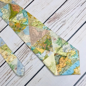 Tie front and end lay parallel angled into the corner of the frame. Triangle map pieces create a geometric collage or real-world maps. the colores of the maps range from green, tan cream blue, and mustard.